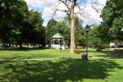 Photo of large open grassy area on Common with leafy trees along the side and Gazebo in background.