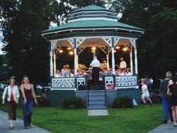 Close-up of Gazebo with conductor and musicians within - showing 2 ladies walking by