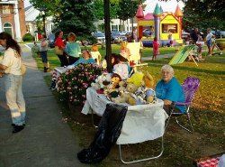 Phot of a table set up alongside a sidewalk featuring stuffed toys - children's bouncey house is in background
