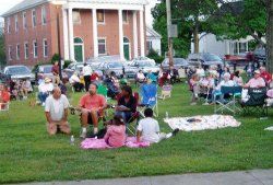 Photo of around 30 people relaxing on large grassy area - some on blankets, some in folding chairs