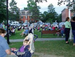 bPhoto of around 30 people relaxing in folding chairs on large grassy area- child in stroller is in the foreground