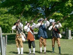 Photo of men dressed in Revolutionary garb pointing muskets upward